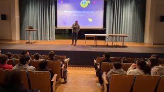 Junghandwerker Mann spricht vor Publikum in einem Vortrag über Handwerksberufe