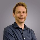 Zeitschriften Porträt eines lächelnden Mannes mit blauem Hemd vor grauem Hintergrund