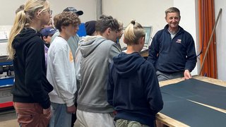 Junghandwerker Gruppe Jugendlicher hört einem Mann bei einer Vorführung in einer Werkstatt zu