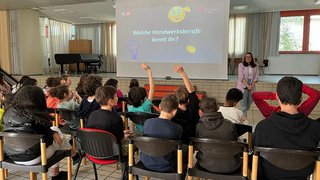 Junghandwerker Schüler heben Hände in einem Klassenzimmer vor einer Präsentation über Handwerksberufe