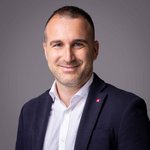 Das lvh-Team Porträt eines lächelnden Mannes in weißem Hemd und dunkelblauem Sakko vor grauem Hintergrund