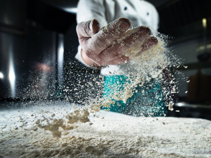 Bäcker Koch wirft Mehl in die Luft in professioneller Küche