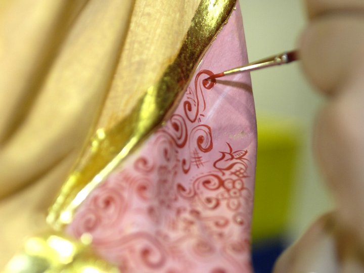 Fassmaler und Vergolder Nahaufnahme einer Hand, die filigrane rote Muster auf rosa Oberfläche malt