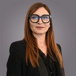 Das lvh-Team Porträt einer Frau mit langen roten Haaren und schwarzer Kleidung vor grauem Hintergrund