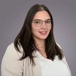 Das lvh-Team Porträt einer lächelnden Frau mit langen braunen Haaren und Brille vor grauem Hintergrund