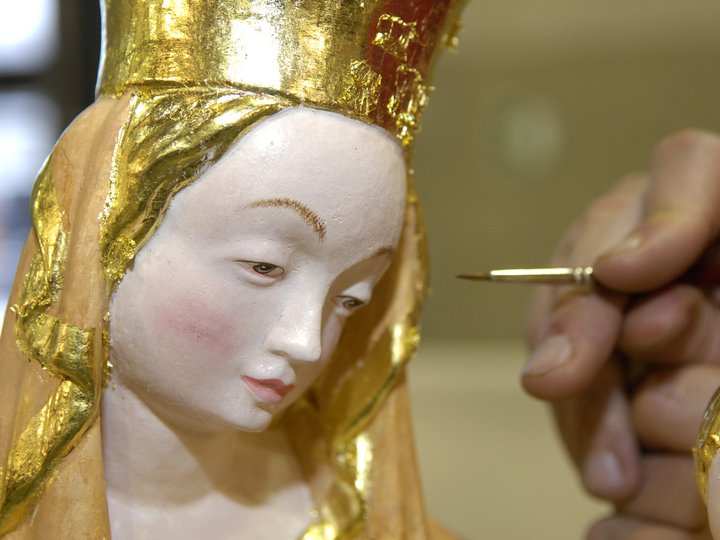 Fassmaler und Vergolder Hand malt feine Details an traditionelle religiöse Statue mit Goldverzierung