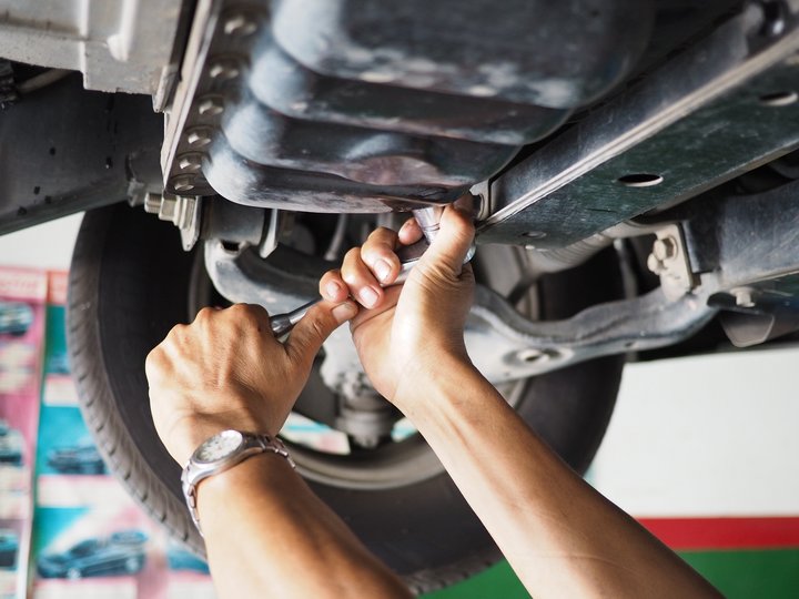 Kfz-Mechatroniker Hände eines Mechanikers, die unter einem Auto mit einem Schraubenschlüssel arbeiten