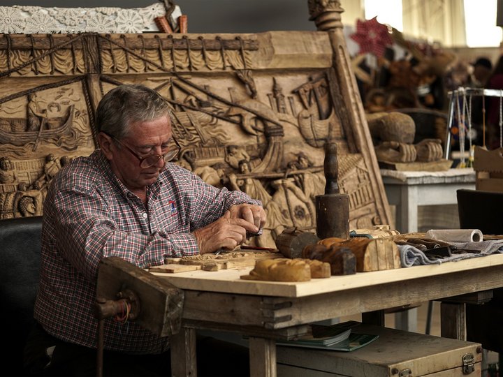 Verzierungsbildhauer Älterer Mann schnitzt Holz mit Werkzeugen an einem Arbeitstisch