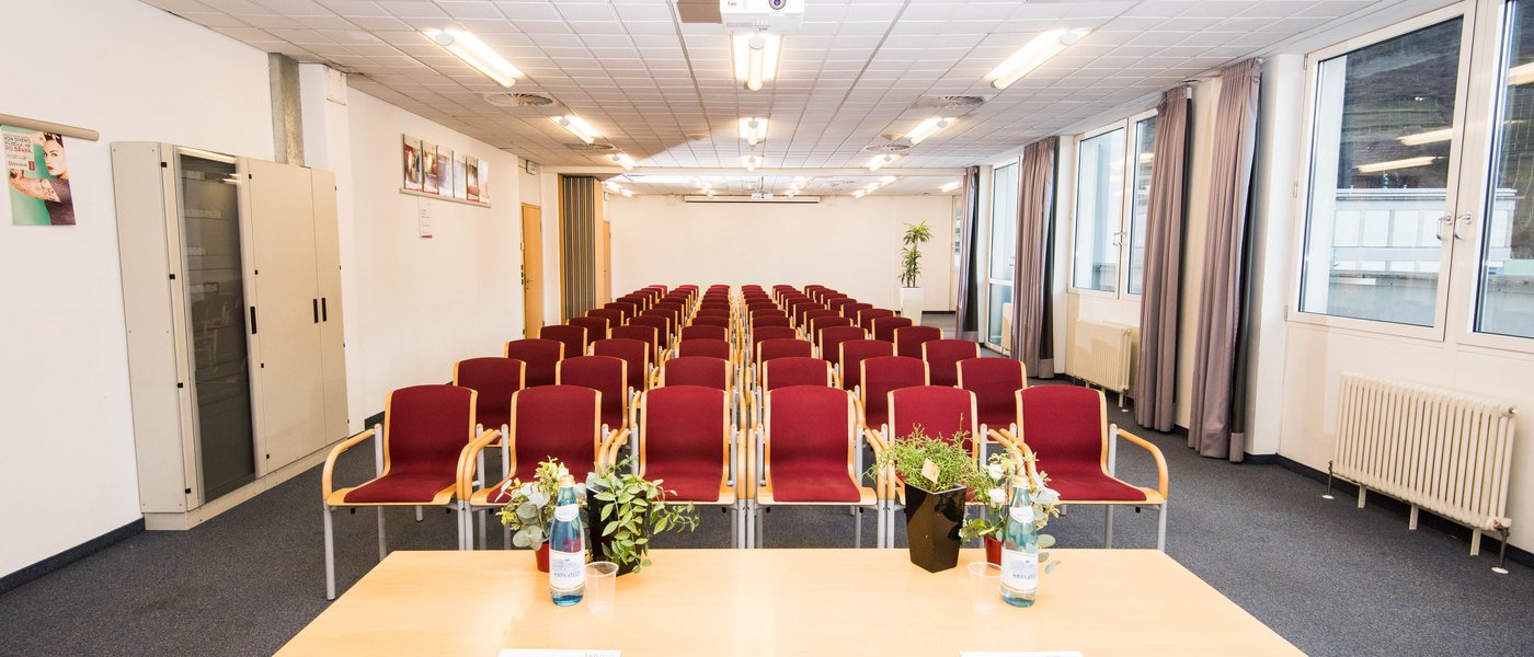 Vermietung Seminarräume Leerer Konferenzraum mit roten Stühlen, Tisch mit Wasserflaschen und Pflanzen