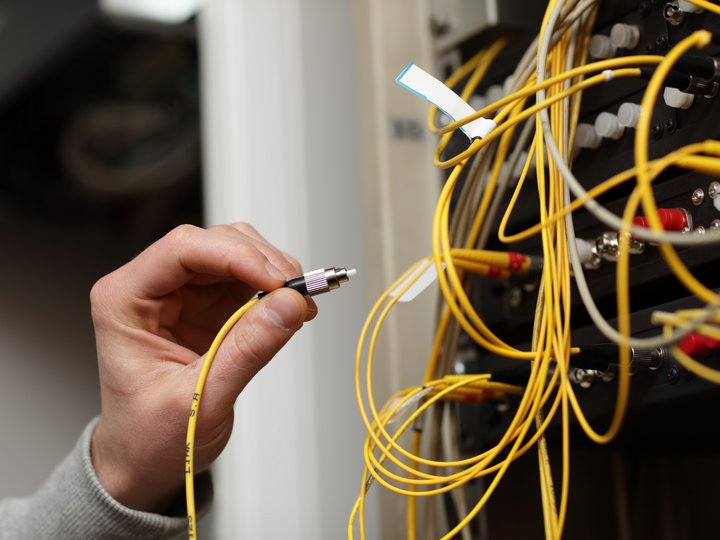 Kommunikationstechniker Hand hält ein gelbes Glasfaserkabel neben einem Netzwerkanschluss