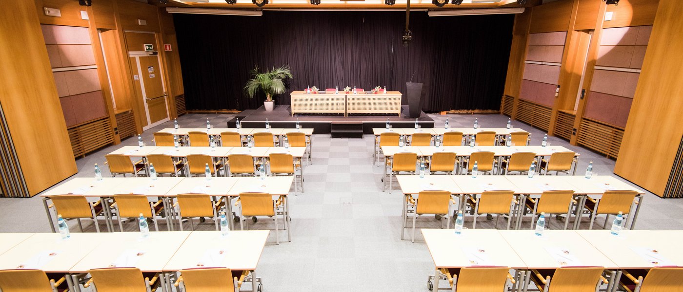 Vermietung Seminarräume Konferenzraum mit Stuhlreihen und Bühne mit schwarzen Vorhängen