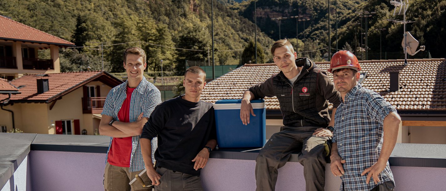 Junghandwerker Vier Bauarbeiter posieren auf einem Dach mit Bergen im Hintergrund