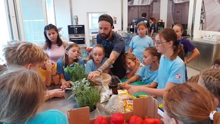 Junghandwerker Kinder und Mann lernen in einer Küche mit frischen Paprikaschoten und Kräutern