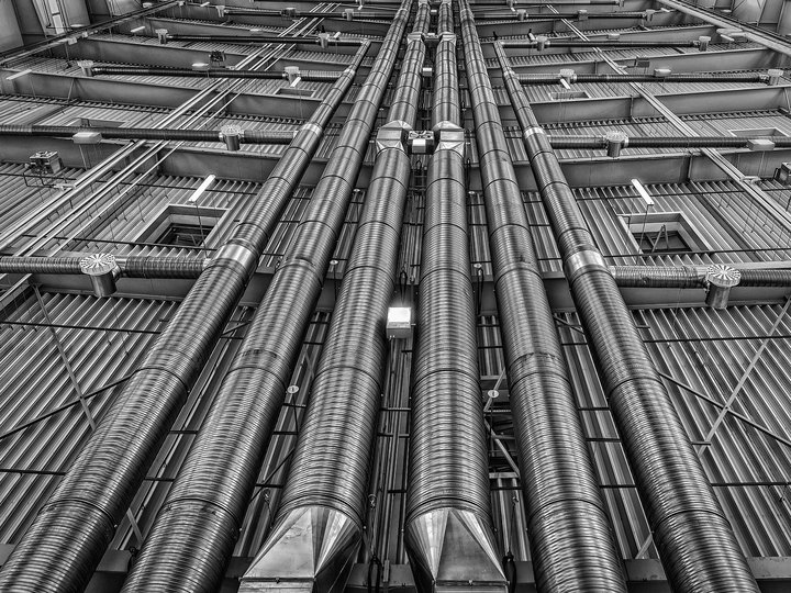 Kälte- und Klimatechniker Blick nach oben auf große industrielle Metallrohre an einer Lagerhallenwand