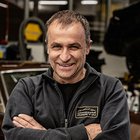 Karosserietechniker Lächelnder Mann in schwarzer Jacke mit verschränkten Armen in Werkstatt