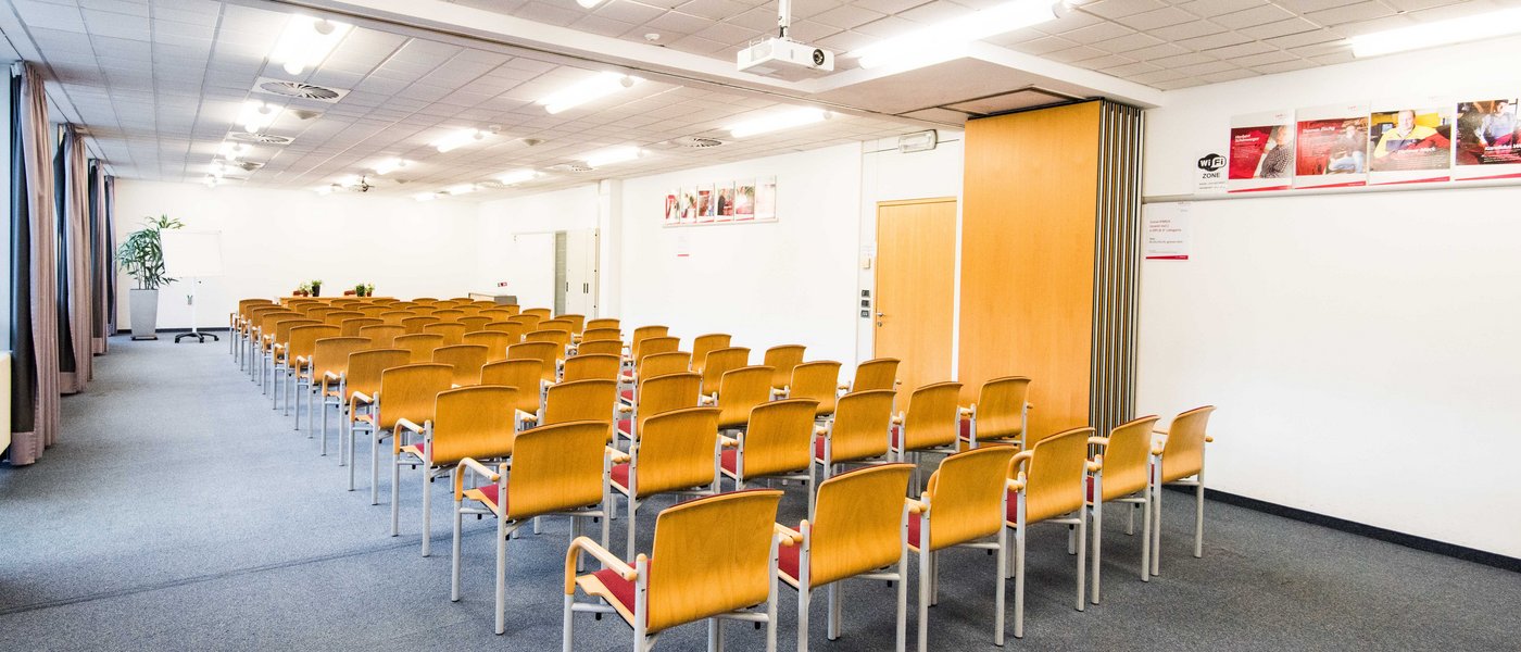 Vermietung Seminarräume Leerer heller Konferenzraum mit mehreren Reihen von Holzstühlen