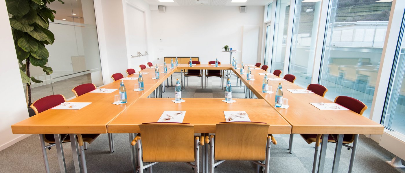 Vermietung Seminarräume Konferenzraum mit U-förmigen Tischen, Stühlen und Wasserflaschen an jedem Platz