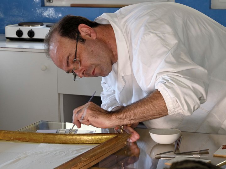 Restauratoren Mann in weißem Kittel restauriert einen goldenen Bilderrahmen