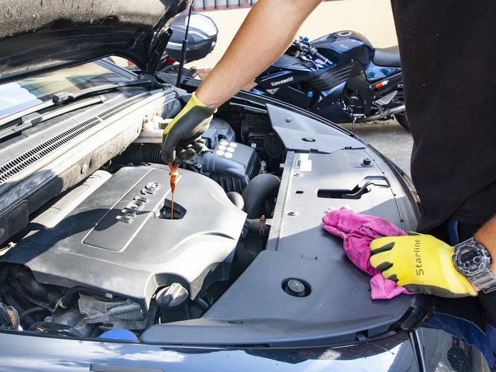 Kfz-Mechatroniker Person prüft Motorölstand eines Autos mit gelben Handschuhen