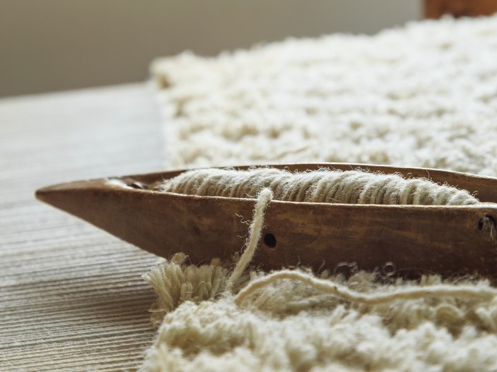 Sticker, Stricker und Weber Altes Holzweberschiffchen mit aufgewickeltem Garn auf einem gewebten Stoff