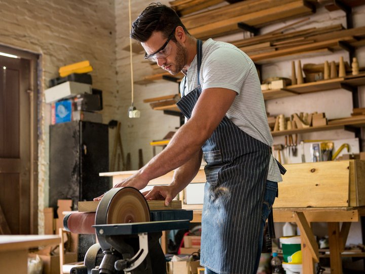 Tischler Mann schleift Holz in einer Werkstatt mit Schutzbrille und Schürze