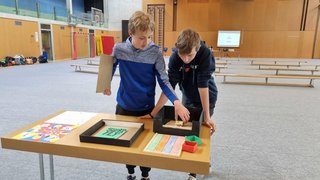 Junghandwerker Zwei Jungen spielen an einem Tisch mit bunten Spielmaterialien in einer Turnhalle