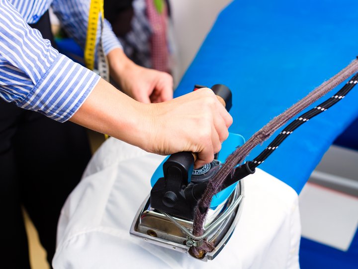 Textilreiniger Person bügelt Hemd mit professionellem Bügeleisen