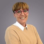 Das lvh-Team Lächelnde Frau mit kurzen blonden Haaren und roten Brillen vor grauem Hintergrund