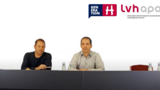 Webinare Zwei Männer sitzen an einem Tisch bei einer Podiumsdiskussion mit Logo im Hintergrund