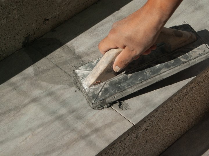 Fliesen-, Platten- und Mosaikleger Hand glättet Beton auf Treppenstufe mit Glättkelle