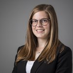 Das lvh-Team Porträt einer lächelnden Frau mit Brille und langem braunem Haar vor grauem Hintergrund