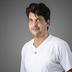 Das lvh-Team Porträt eines Mannes mit weißem T-Shirt und Anhänger vor grauem Hintergrund