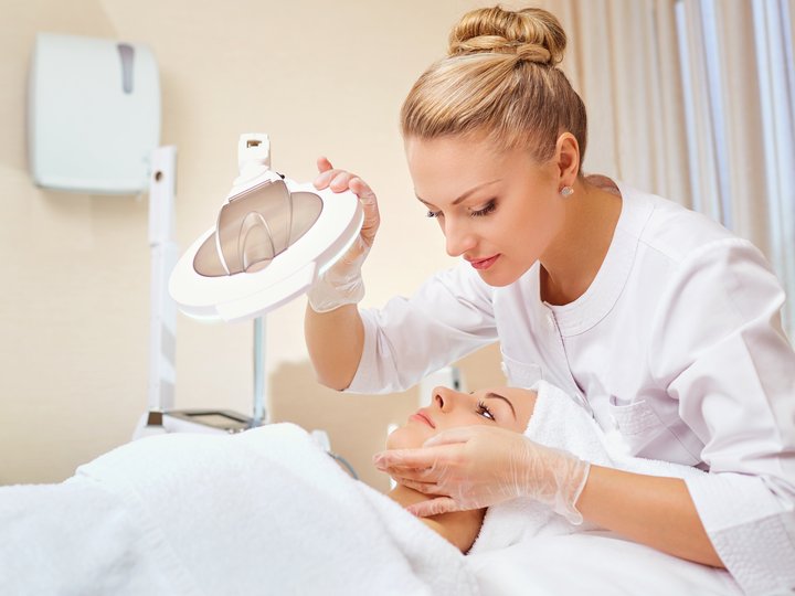 Schönheitspfleger Kosmetikerin untersucht Gesicht einer Frau mit Lupe in einem Spa