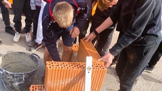 Junghandwerker Jugendliche mauern mit Ziegelsteinen und verwenden Wasserwaage