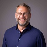 Das lvh-Team Lächelnder Mann mit Brille und blauem Hemd vor grauem Hintergrund