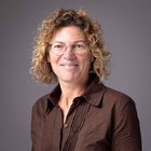 Unfall und Krankheit Porträt einer Frau mit lockigen Haaren und Brille vor grauem Hintergrund