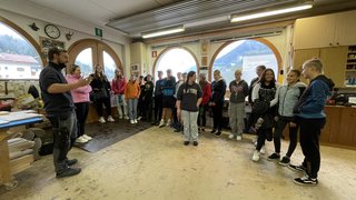 Junghandwerker Gruppe Jugendlicher in Werkstatt, hört einem Mann zu, der vorne spricht