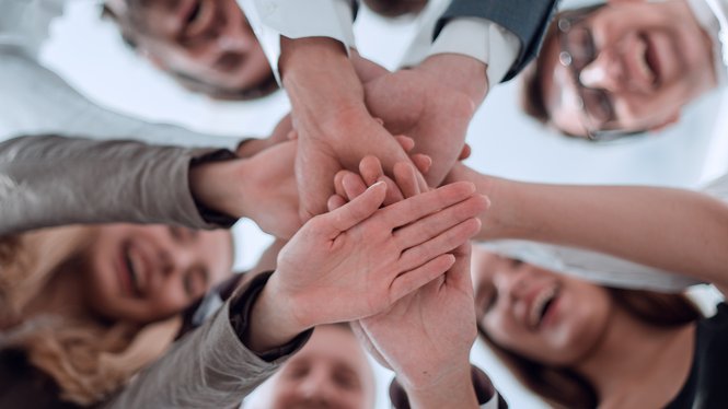 Mitarbeiterbindung Lachende Menschen legen ihre Hände gemeinsam übereinander