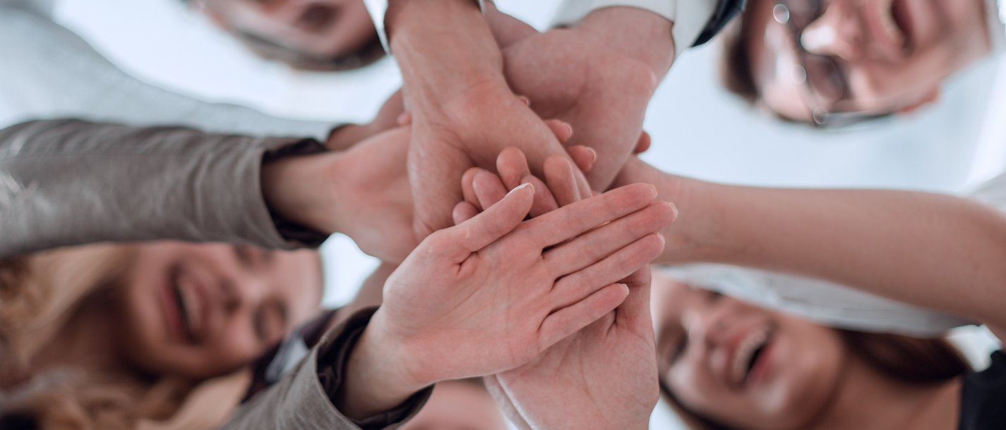 Mitarbeiterbindung Lachende Menschen legen ihre Hände gemeinsam übereinander