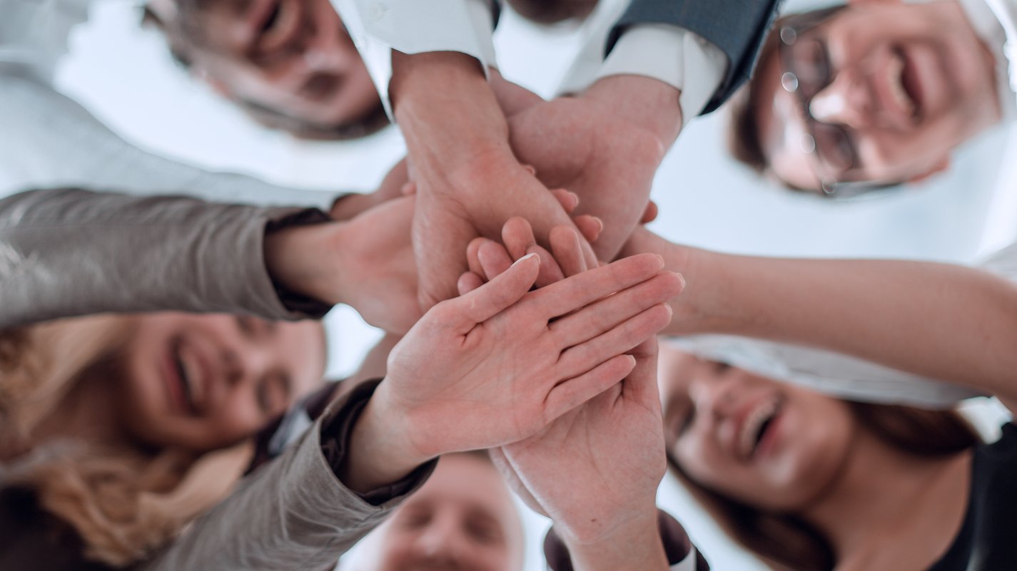 Mitarbeiterbindung Lachende Menschen legen ihre Hände gemeinsam übereinander