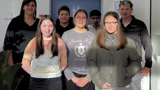 Junghandwerker Gruppe von sieben Personen steht vor einer blauen Tür in einem hellen Raum