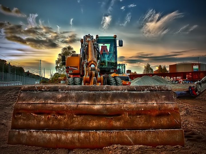Tiefbauunternehmer Baubagger mit großer Schaufel vor dramatischem Himmel auf Baustelle