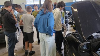 Junghandwerker Gruppe von Jugendlichen betrachtet Motorraum eines Autos in Werkstatt