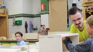 Junghandwerker Lehrer unterstützt Kinder beim Holzarbeiten in einer Werkstatt