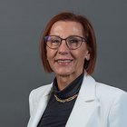 Medien Porträt einer Frau mit Brille, weißem Blazer und kurzem roten Haar vor grauem Hintergrund