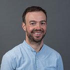 Hafner Porträt eines lächelnden Mannes mit kurzem Bart vor grauem Hintergrund