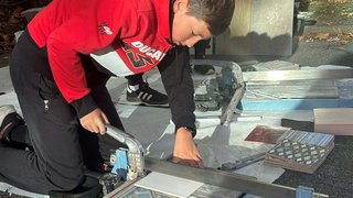 Junghandwerker Junge schneidet Fliesen mit Fliesenschneider im Freien