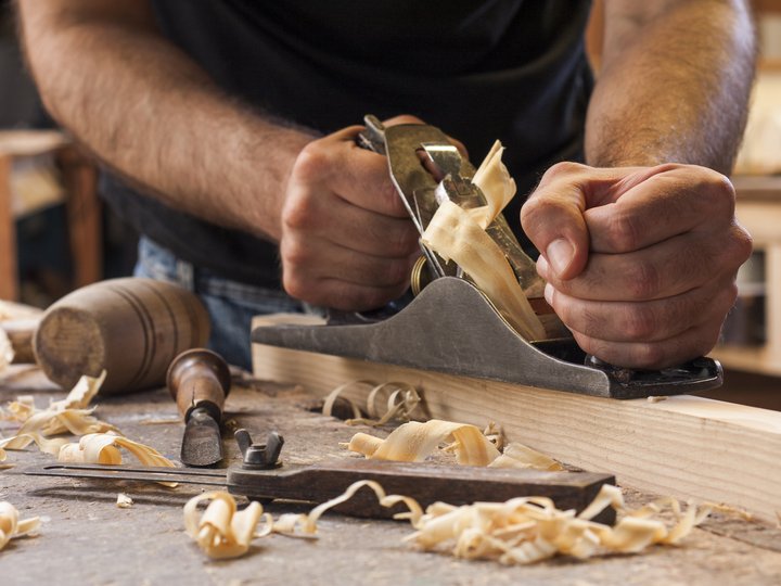 Tischler Handwerker hobelt Holz mit Hobel auf Werkbank voller Holzspäne