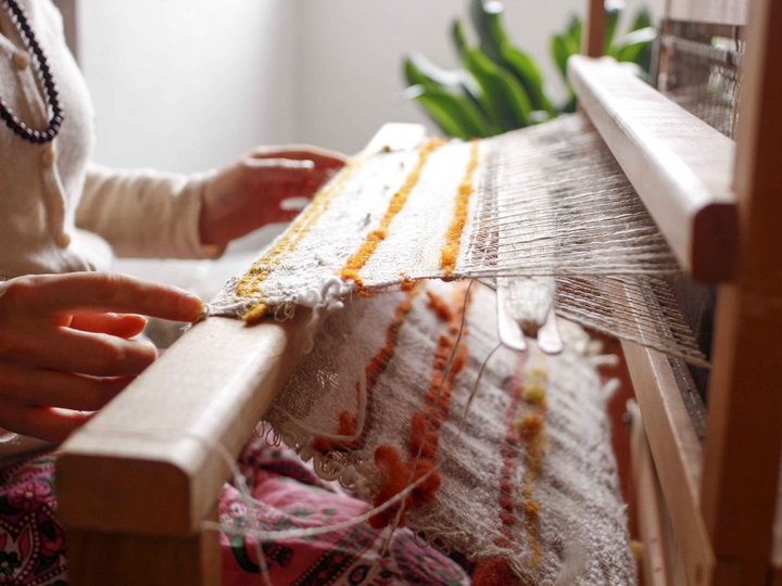 Sticker, Stricker und Weber Person webt auf einem Webstuhl mit buntem Garn in einem hellen Raum