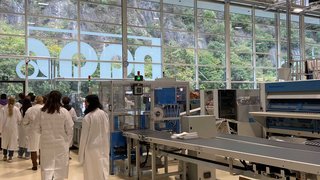 Junghandwerker Menschen in weißen Kitteln in einer Fabrikhalle mit Maschinen und Kartons